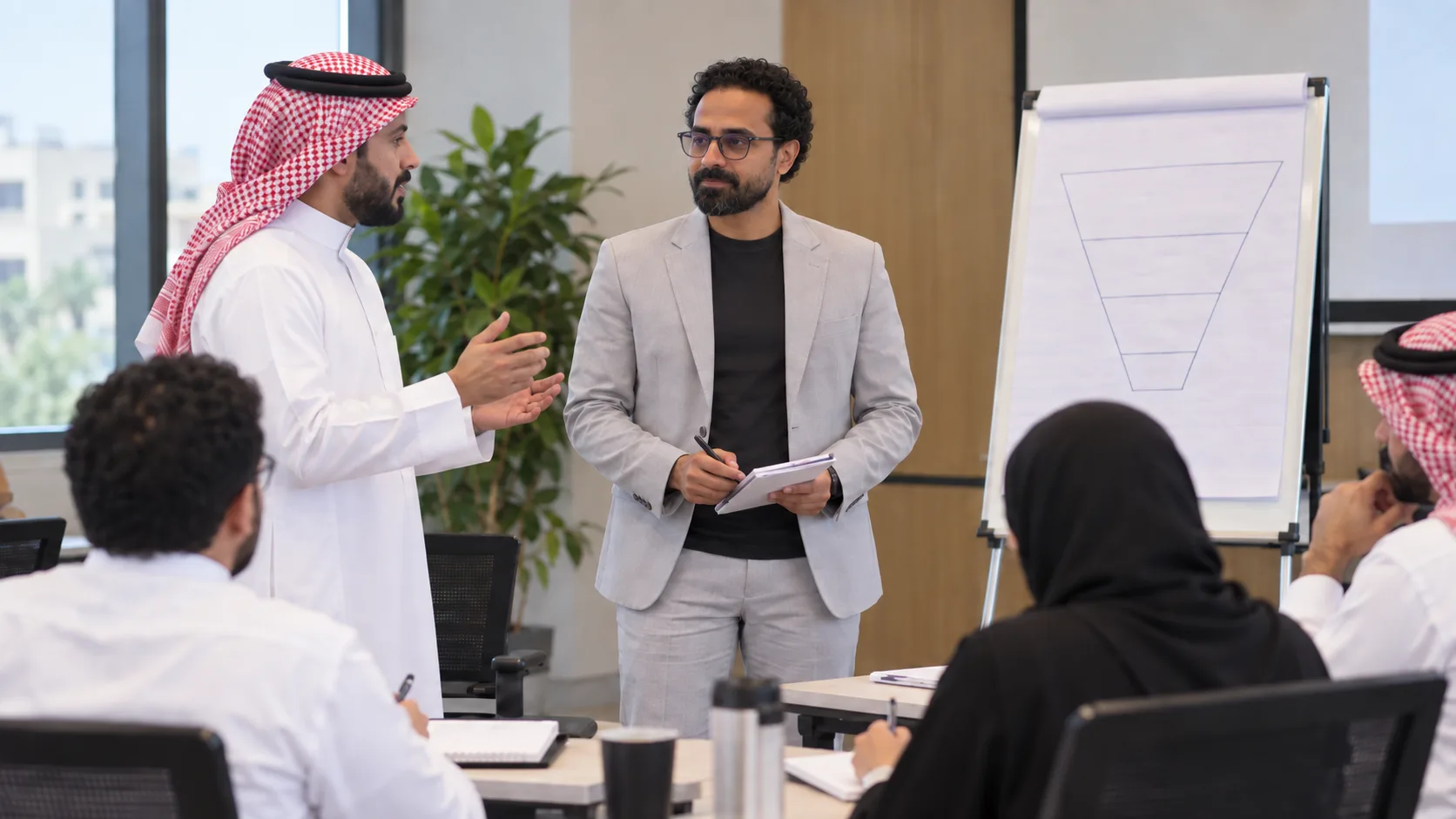 During a workshop, Ashraf Ibrahim explains a flip-chart diagram to participants seated around the table
